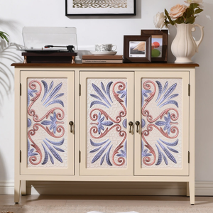 A beige cabinet with floral-patterned doors holds a record player, decorative items, and a vase with flowers on top. A framed wall art piece hangs above, and an open magazine lies on the floor nearby.