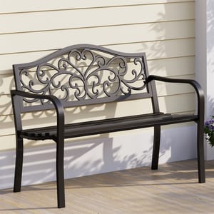 Black cast iron patio bench with an intricate scroll pattern on the backrest, featuring curved armrests, and positioned on a wooden deck against a light-colored wall.