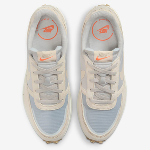 A pair of beige and light blue Nike sneakers with orange brand logos on the insoles.