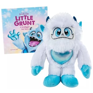A white and blue plush Yeti with a shimmering heart stands next to a book titled \“Little Grunt: A SnoBiggie Yeti Story\“ by Chanda A. Bell.