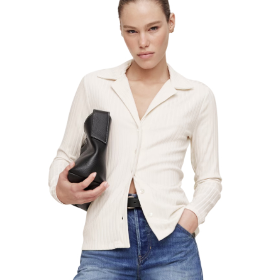 Woman wearing a white button-up shirt and blue jeans holds a black handbag.