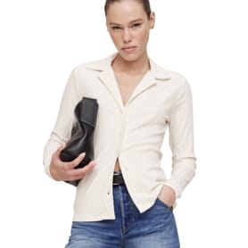 Woman wearing a white button-up shirt and blue jeans holds a black handbag.