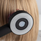 A close-up of a hairbrush with a circular design and bristles is shown brushing through straight, blonde hair.