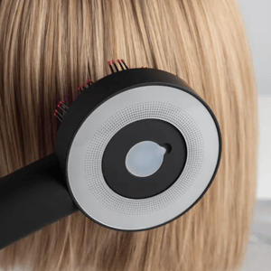 A close-up of a hairbrush with a circular design and bristles is shown brushing through straight, blonde hair.