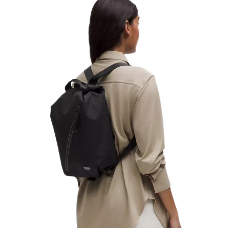 A person is wearing a black, minimalist backpack with a front zipper, over a beige shirt.