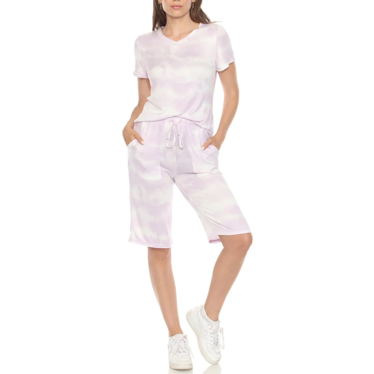 A woman is wearing a light purple tie-dye V-neck T-shirt and matching knee-length drawstring shorts with white sneakers.