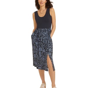 A woman is wearing a sleeveless dress with a solid black top and a blue floral-patterned skirt featuring a side slit, paired with light-colored woven shoes.