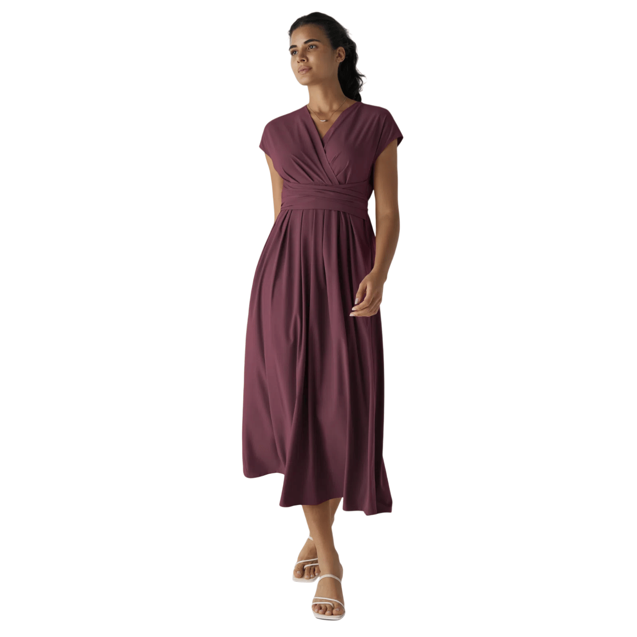 A woman is wearing a plum-colored, V-neck, short-sleeve wrap dress with an empire waist, paired with white strappy sandals.