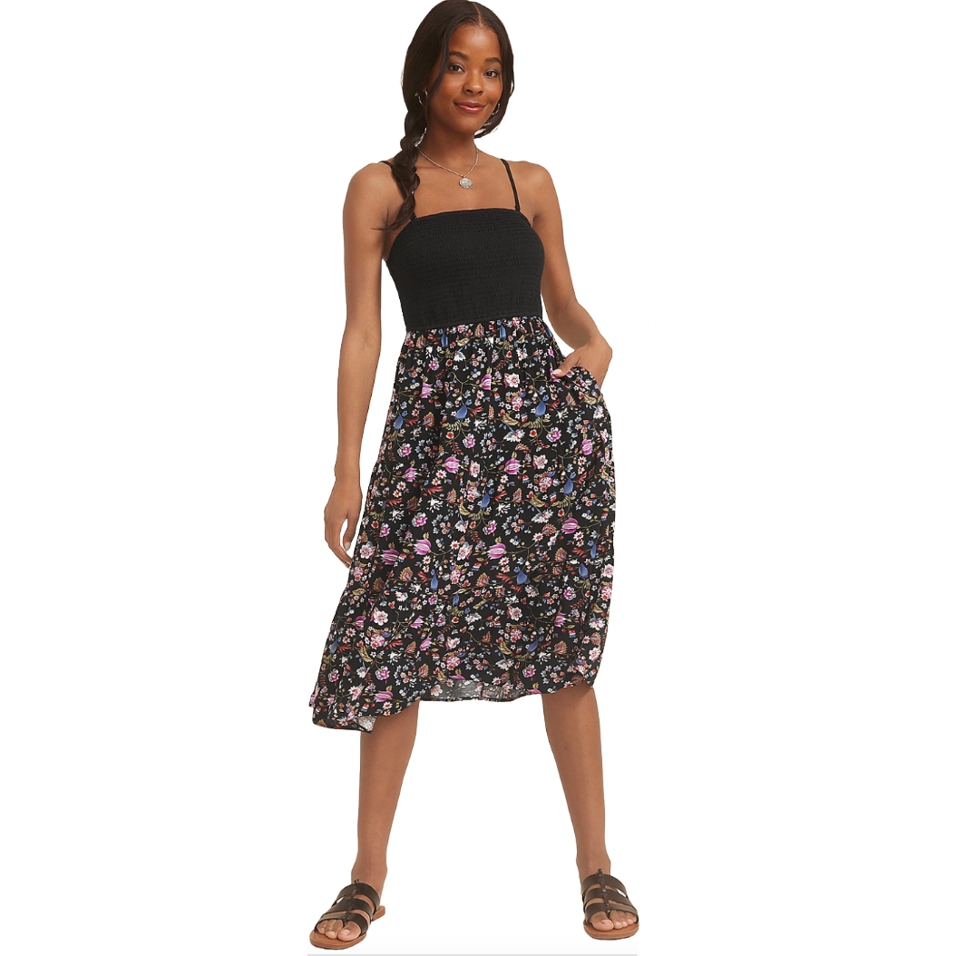 Black midi dress with a smocked, strapless bodice and spaghetti straps, featuring a floral print in pink, blue, and purple hues. Paired with brown sandals, the dress includes side pockets and has a casual, summery look.