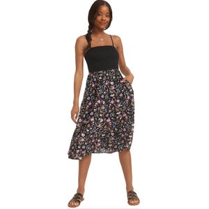 Black midi dress with a smocked, strapless bodice and spaghetti straps, featuring a floral print in pink, blue, and purple hues. Paired with brown sandals, the dress includes side pockets and has a casual, summery look.