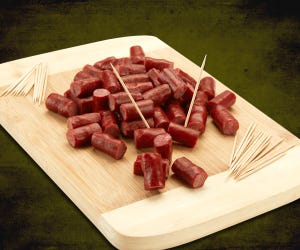 A wooden board displays numerous small sausage pieces with multiple toothpicks inserted, ready for serving.