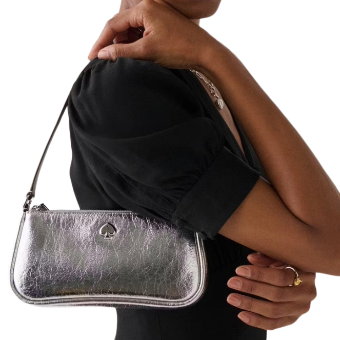 A silver handbag with a spade logo is held by a person wearing a black outfit.