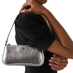 A silver handbag with a spade logo is held by a person wearing a black outfit.