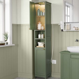 A tall, green bathroom cabinet with shelves containing toiletries and towels is set against light green paneling. It features an open section with bottles and a lower compartment with a door.