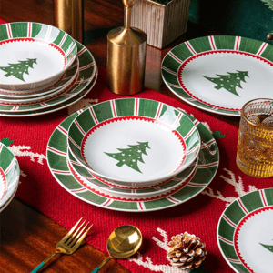 Christmas-themed tableware set with plates and bowls featuring green and red patterns and Christmas tree designs, accompanied by gold utensils and a textured glass on a festive red table runner.