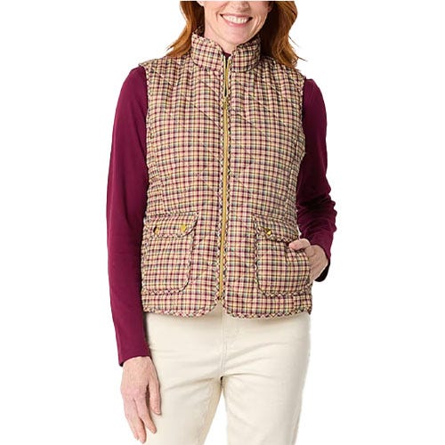 A woman is wearing a plaid quilted vest with a zip-up front and two buttoned pockets, over a long-sleeve burgundy shirt, paired with light-colored pants.