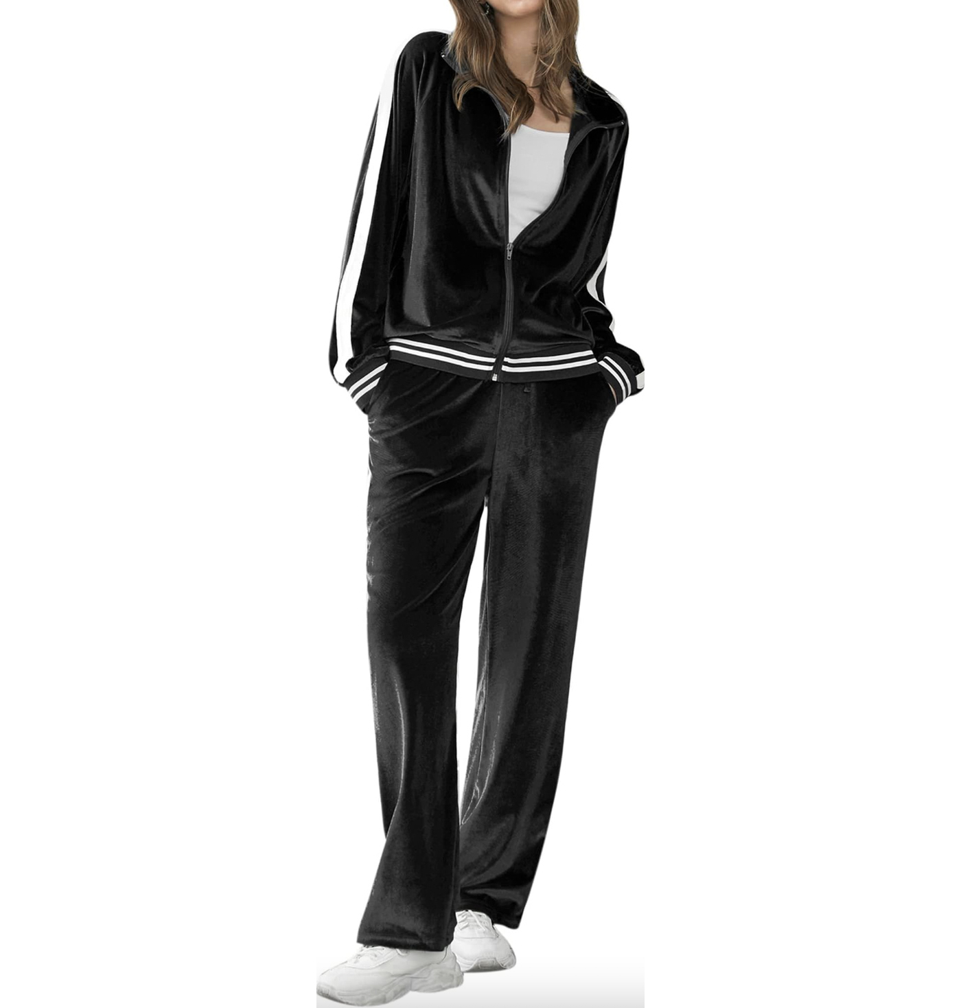 A woman is wearing a black velour tracksuit with a zip-up jacket and contrasting white stripes along the sleeves and trouser sides; she is paired with white sneakers.