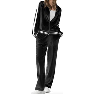 A woman is wearing a black velour tracksuit with a zip-up jacket and contrasting white stripes along the sleeves and trouser sides; she is paired with white sneakers.