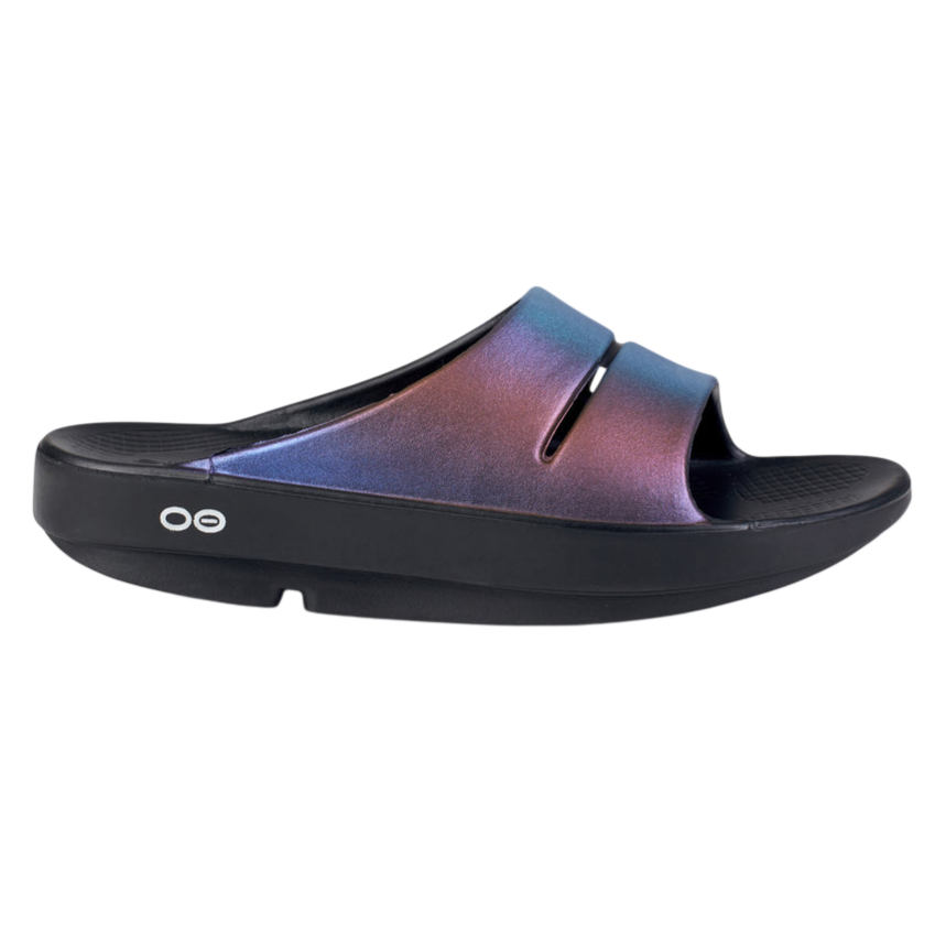 A black slide sandal with a shimmering, multicolored strap. The sandal features a thick sole with a simple branding logo on the side.