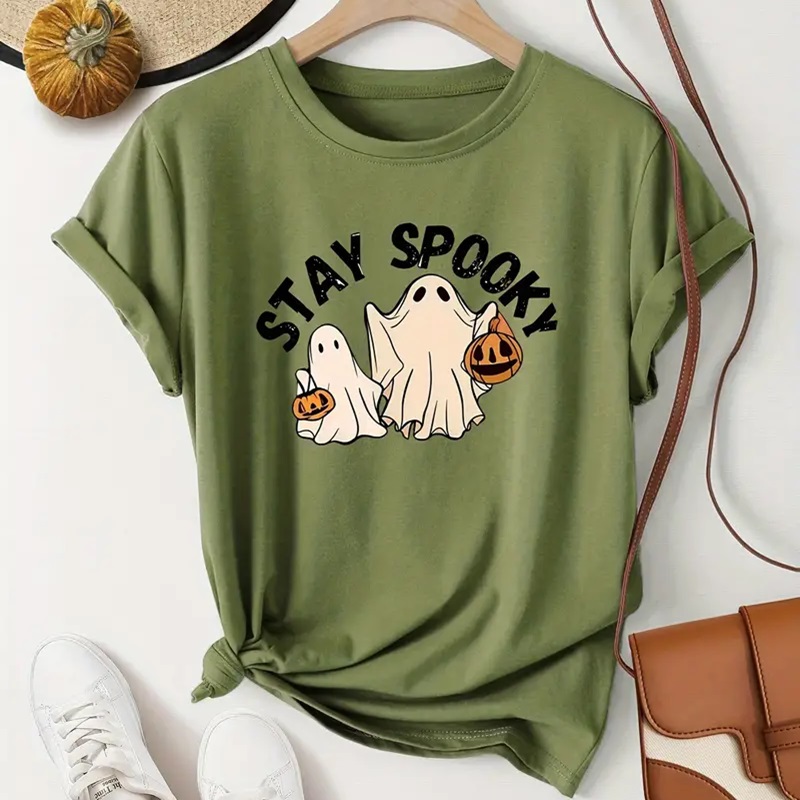 A green t-shirt with a 'Stay Spooky' slogan and three cartoon ghosts, accompanied by a pair of white sneakers and a tan shoulder bag.