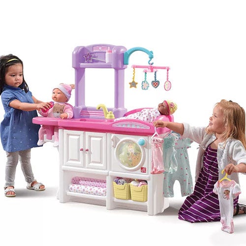 Children are playing with a nursery playset featuring baby dolls, a changing station, and various accessories like clothing and toys.