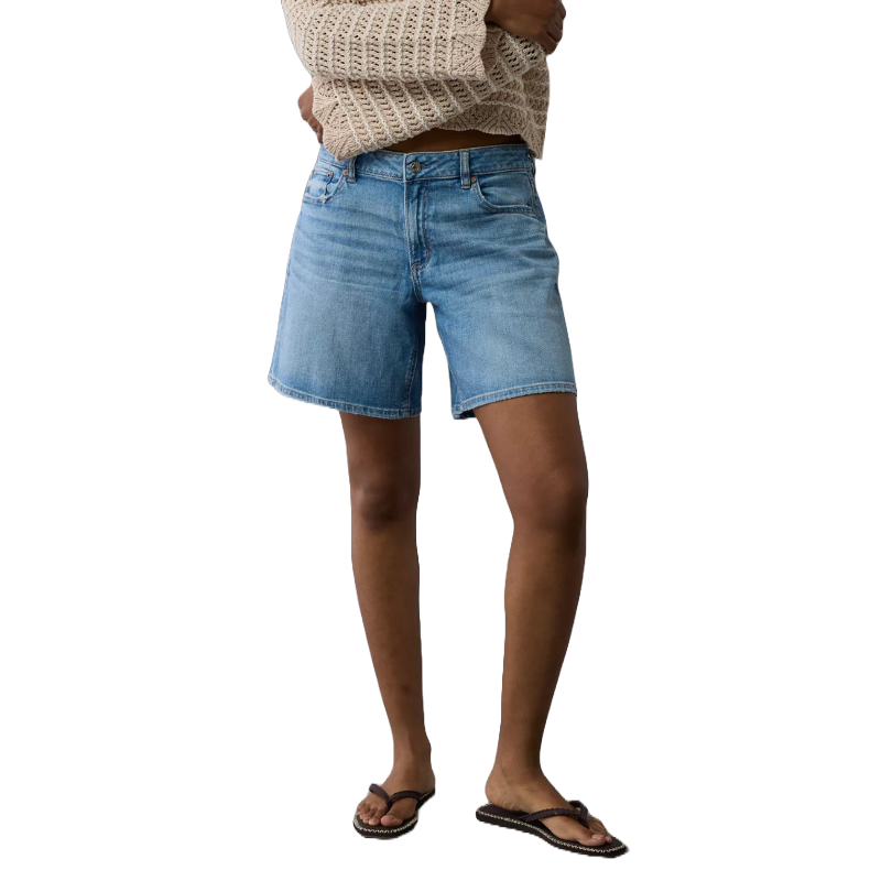 Low-rise, baggy denim shorts in a light blue wash, featuring a relaxed fit. Paired with a cream knit top and flip-flops for a casual look.