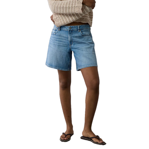 Low-rise, baggy denim shorts in a light blue wash, featuring a relaxed fit. Paired with a cream knit top and flip-flops for a casual look.