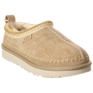 A tan UGG slip-on shoe featuring a suede upper, shearling lining, decorative stitching, and a sturdy rubber sole.