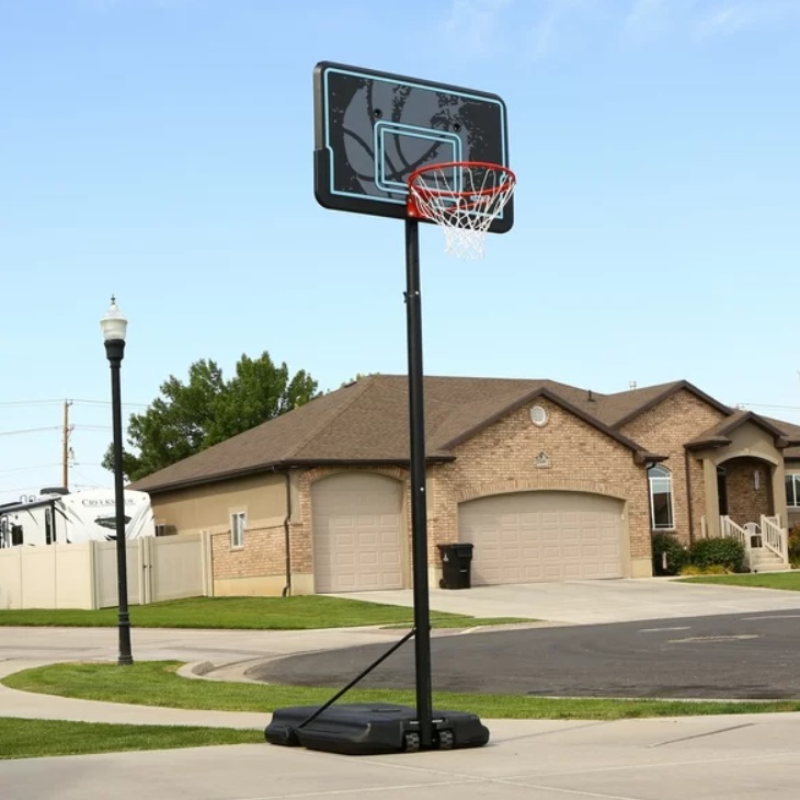 Portable basketball hoop system with a black base and clear backboard on a suburban street.