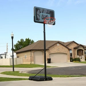Portable basketball hoop system with a black base and clear backboard on a suburban street.