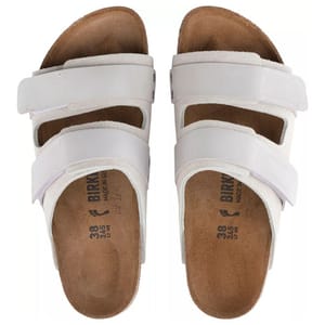 Birkenstock Uji Sandals are white sandals with two adjustable straps, featuring a contoured cork footbed and suede lining for comfort.