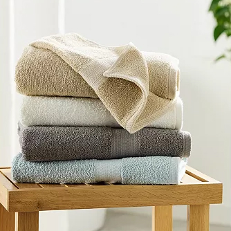 A stack of folded towels in varying shades on a wooden stool.