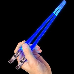 Blue light saber chopsticks are held in a hand, featuring handles designed to resemble the hilts of lightsabers. They emit a bright blue glow along the length of each chopstick.