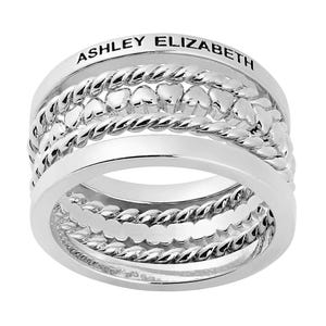 A silver multi-band ring features intricate braided and heart-shaped designs, with the name \“Ashley Elizabeth\“ engraved on the outer band.