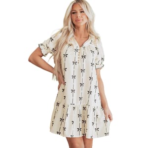 A short, white relaxed-fit dress with black bow prints, featuring short sleeves and a tiered skirt.