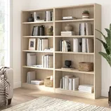 Light wood bookshelves with various books, decorative vases, plants, and woven baskets. A neutral-toned rug and a cozy blanket on a nearby sofa enhance the space.