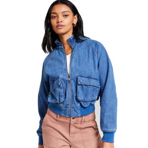 Denim jacket with large front pockets and blue ribbed cuffs and hem, worn over a white top and paired with light brown pants.
