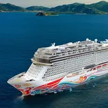 A large cruise ship with colorful decorations sails on the ocean near hilly islands. The ship features multiple decks and outdoor amenities visible on top.