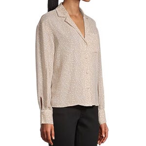 A woman is wearing a long-sleeve, collared button-up blouse with a subtle, light floral pattern, paired with black pants.