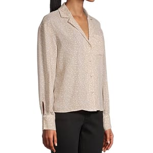 A woman is wearing a long-sleeve, collared button-up blouse with a subtle, light floral pattern, paired with black pants.