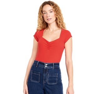 A woman is wearing a red short-sleeve top with a ruched front and square neckline, paired with high-waisted, dark blue denim jeans featuring front pockets.