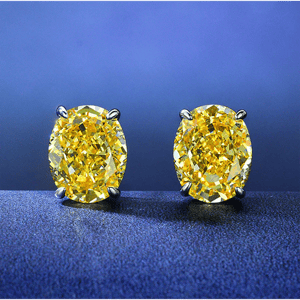 Yellow diamond stud earrings set in prongs, displayed against a blue background.