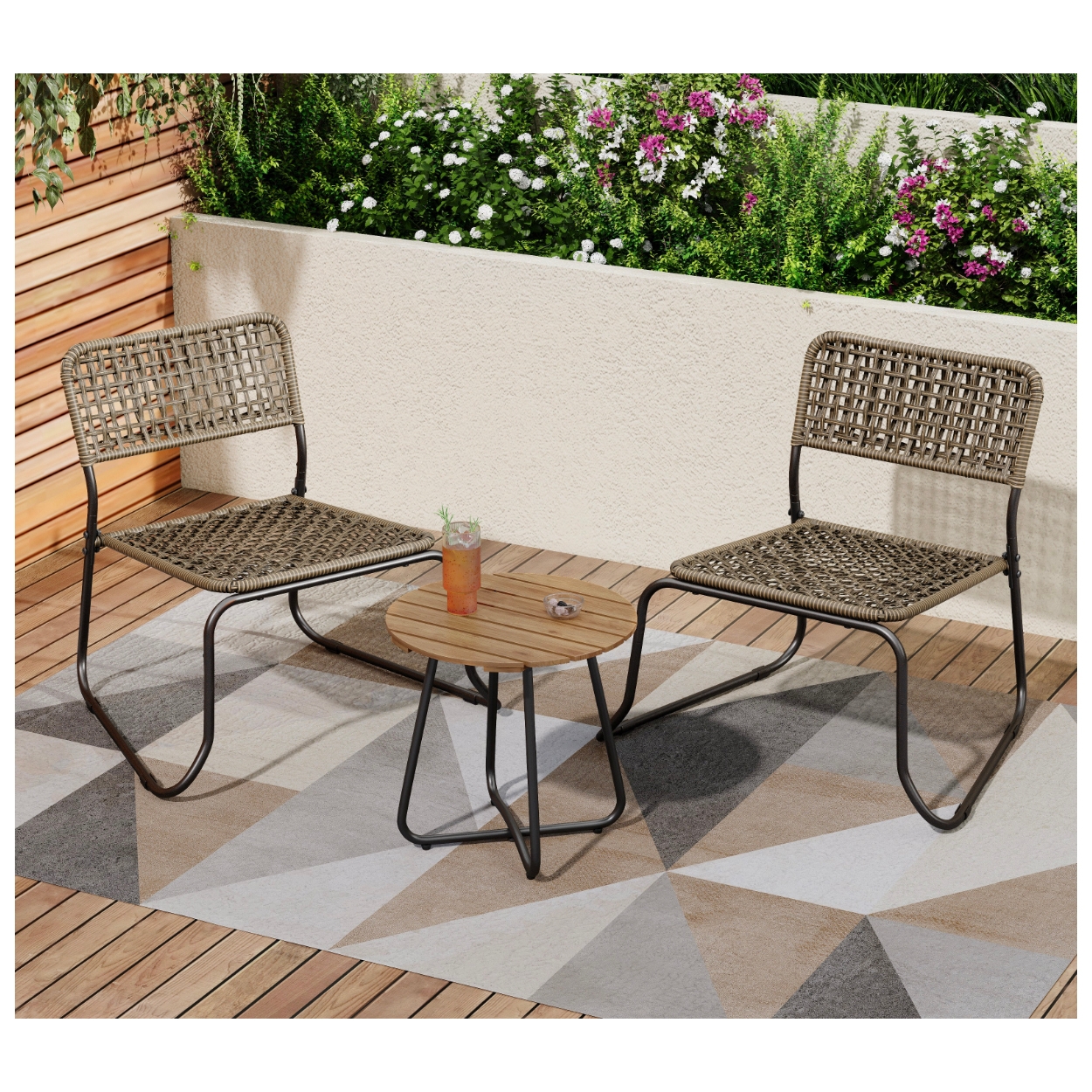 Outdoor seating set with two woven chairs and a small round wooden table on a geometric-patterned outdoor rug, surrounded by greenery and flowers.