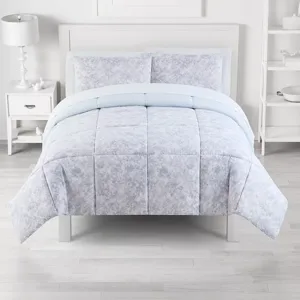 A light blue and white comforter set with a subtle floral pattern is displayed on a neatly made bed. The room features a white nightstand with a lamp and décor, and a shelving unit with various items, all against a minimalist white backdrop.