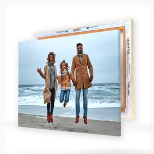 A canvas print featuring a joyful family of three jumping on a beach, with the ocean in the background.