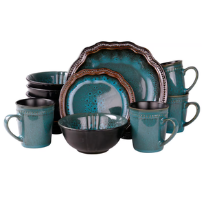 Teal and black stoneware dinnerware set includes scalloped-edge plates, bowls, and mugs with a reactive glaze finish, showcasing a rustic and artistic design.