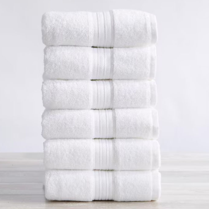 A stack of six neatly folded white towels with a textured stripe pattern placed on a light wooden surface.