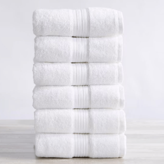 A stack of six neatly folded white towels with a textured stripe pattern placed on a light wooden surface.