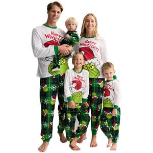 Matching family pajamas with a green Grinch design and \“Happy Wholldays\“ text, featuring green and red accents on a plaid background.