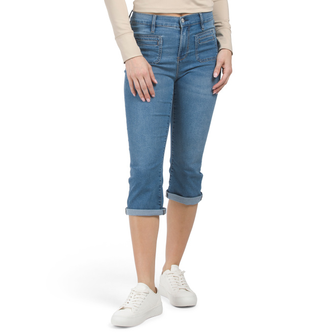 Blue denim capri jeans with a mid-rise waist, rolled-up cuffs, and front and back pockets, paired with a beige long sleeve top and white sneakers.